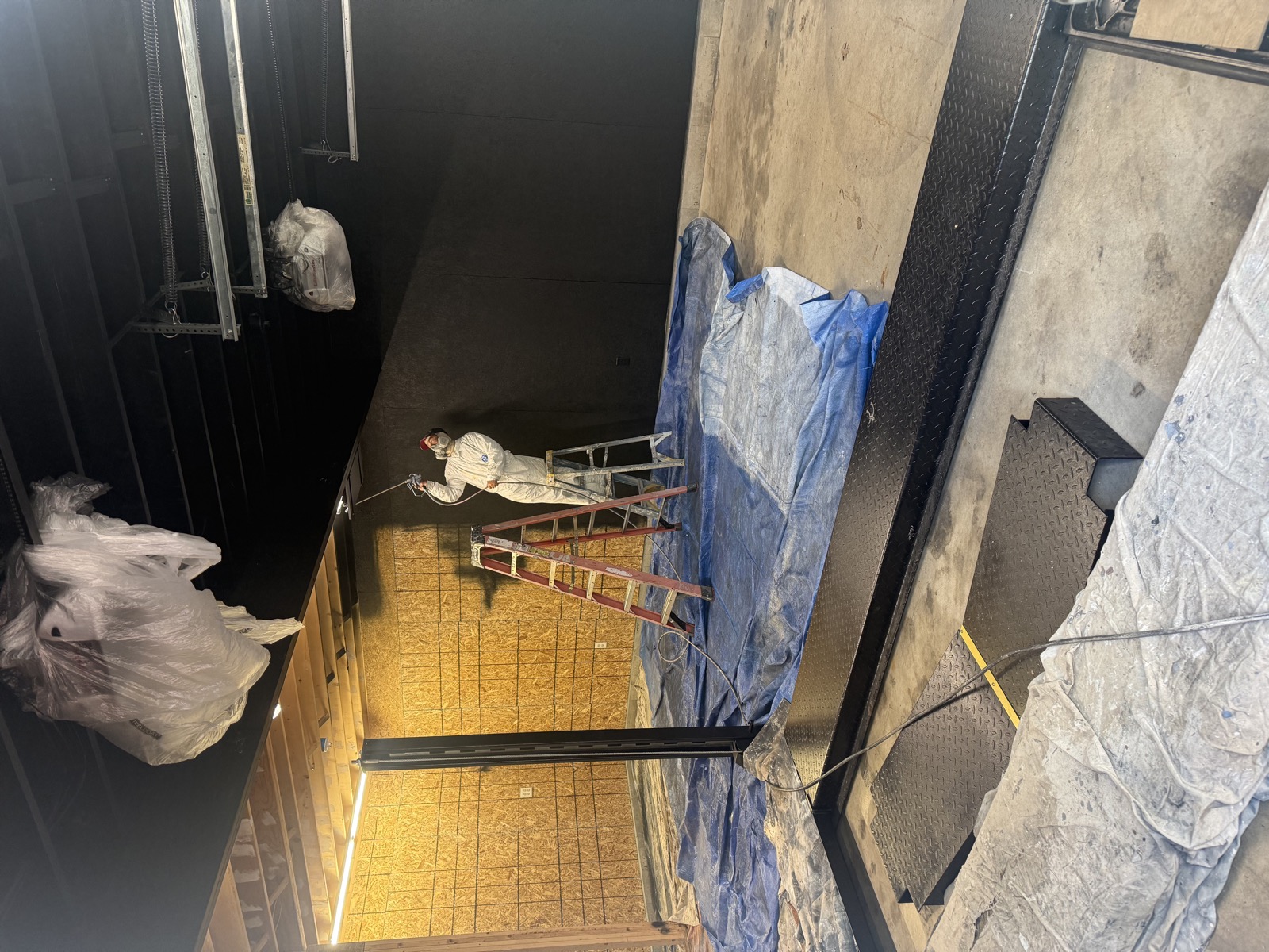 Painter spraying black finish in a garage workshop with floors protected